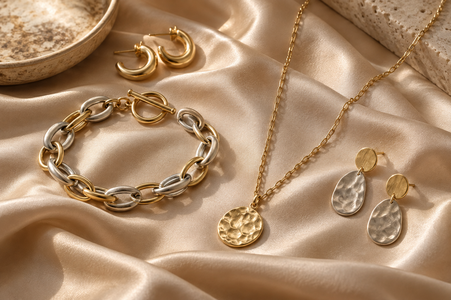 Conceptual silver-toned and gold-toned jewelry on champagne fabric.